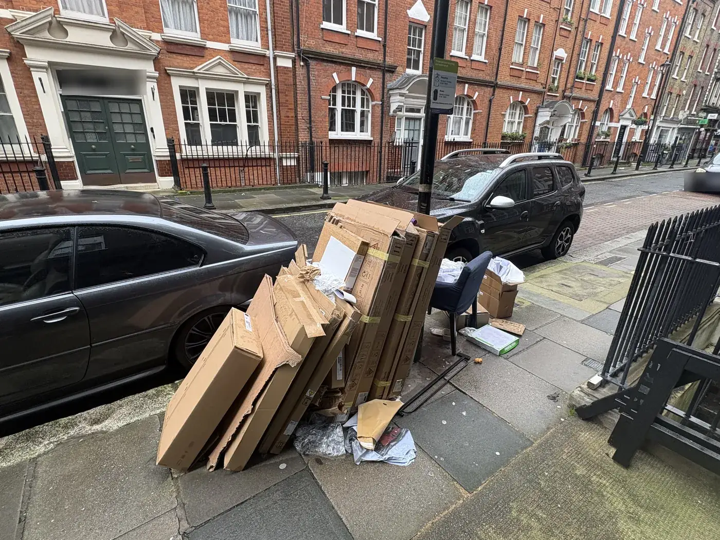 Flattened cardboard boxes, packaging and a chair on the pavement on Hanson Street, Fitzrovia, awaiting collection.