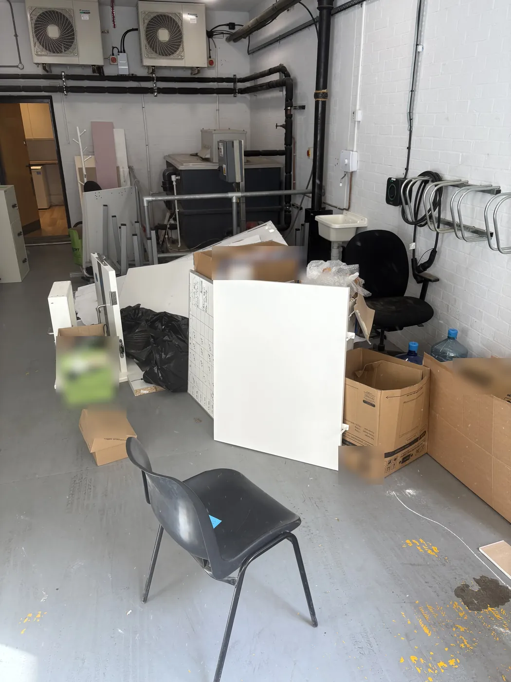 Office chairs, cabinet panels, desk frames, boxes and bagged waste in a basement store on Berners Street, Fitzrovia, before clearance.