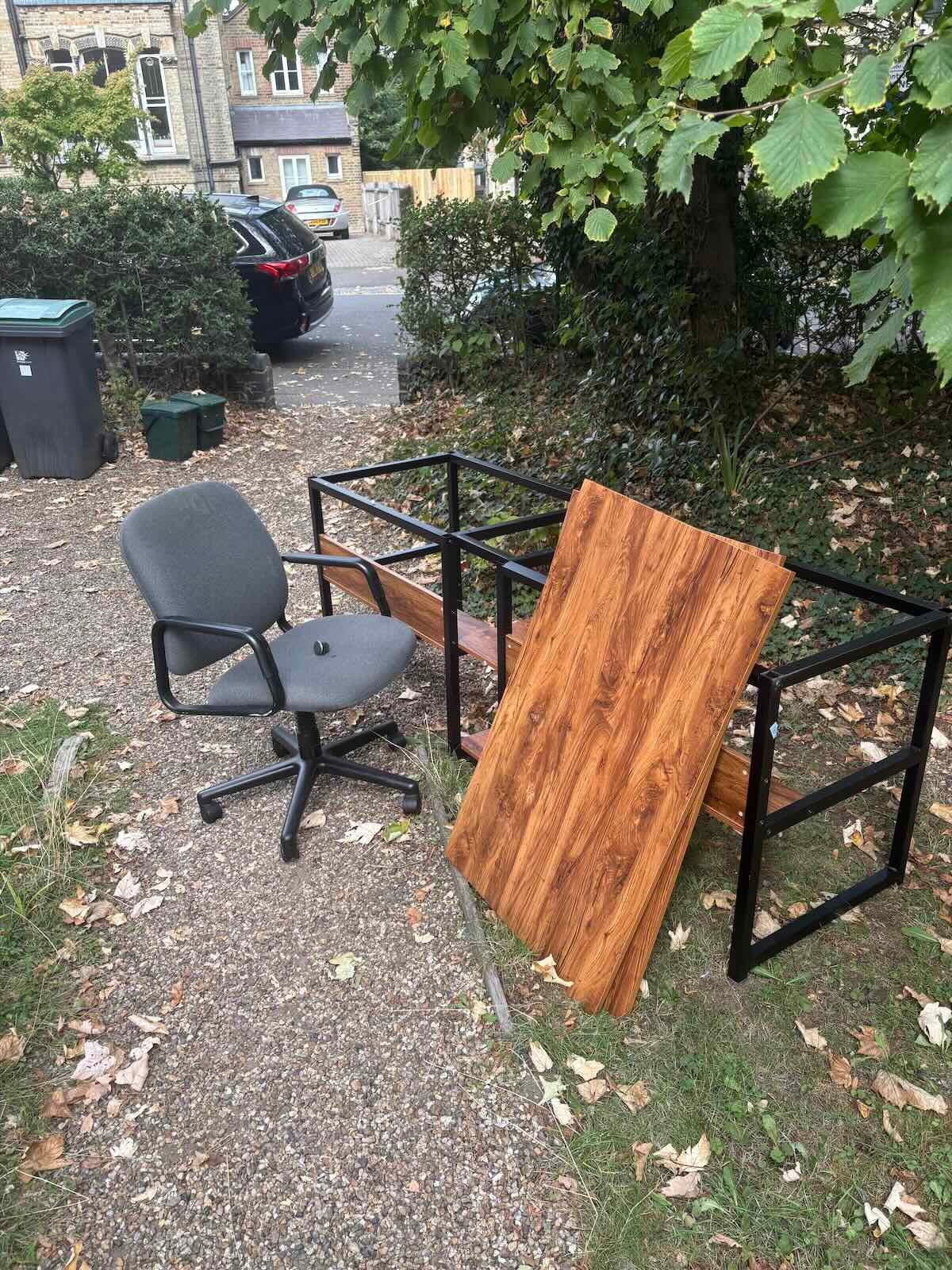 Office chair, black metal desk frame and wooden desktop on a front garden path in Highgate N6 before furniture removal