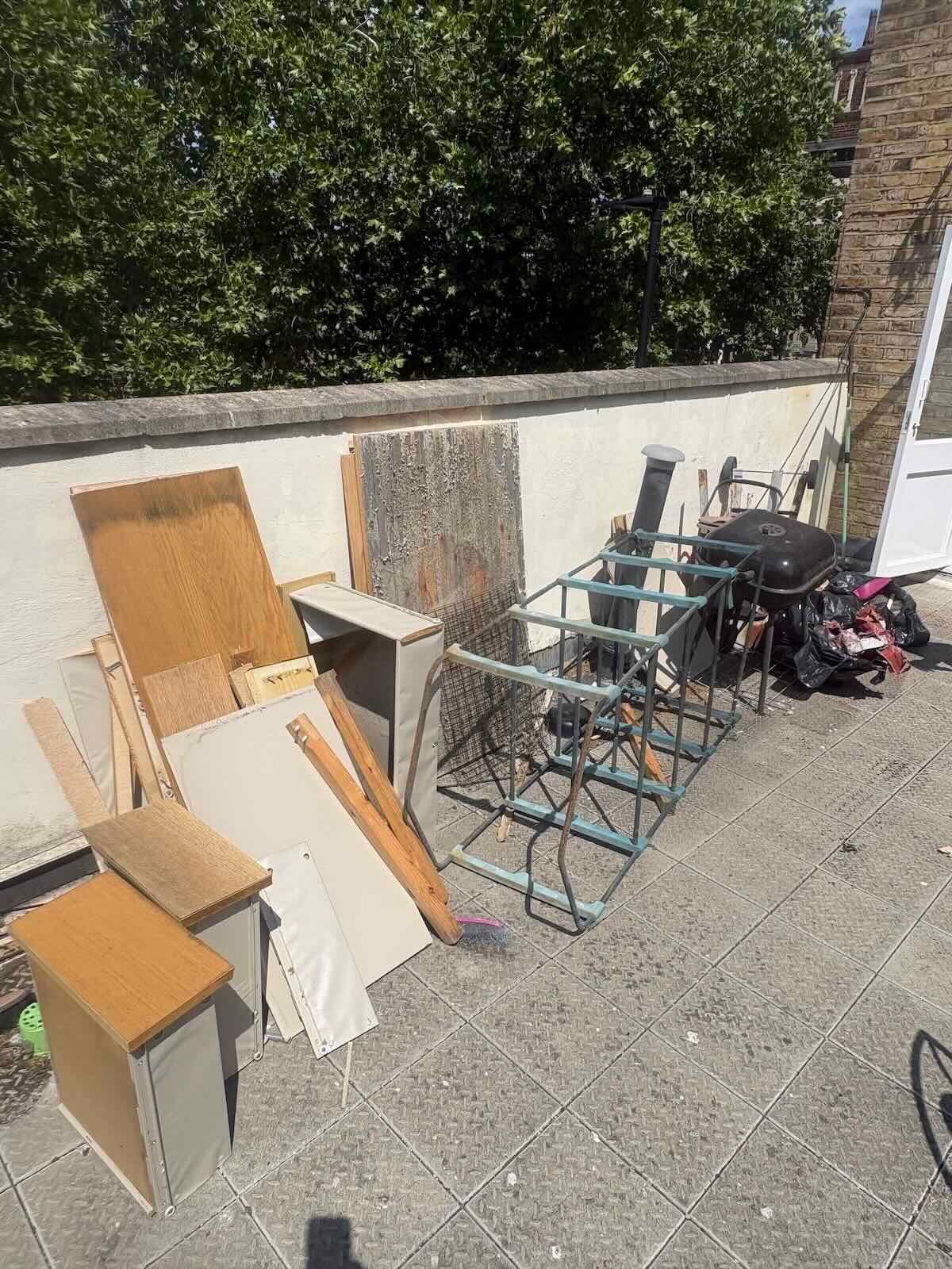 Roof terrace on Burghley Road, Kentish Town NW5 with old chipboard units, timber, a metal frame, BBQ and bagged waste before clearance