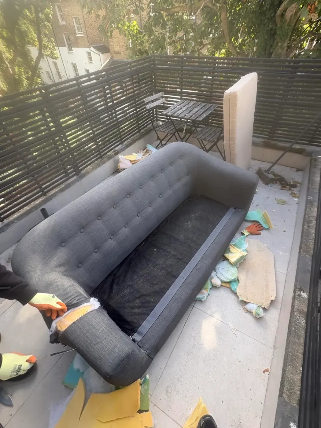 Sofa removal Canonbury N1 before dismantling, with the grey sofa's fabric and foam stripped back on an upper-floor roof terrace